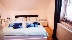 Una cama bien hecha con toallas dobladas, una mesita de noche con lámpara y una ventana con cortinas.