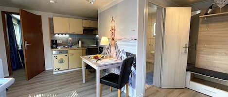 Um espaço compacto com cozinha compacta, área de refeições com mesa e cadeiras, e um banheiro visível por uma porta aberta.