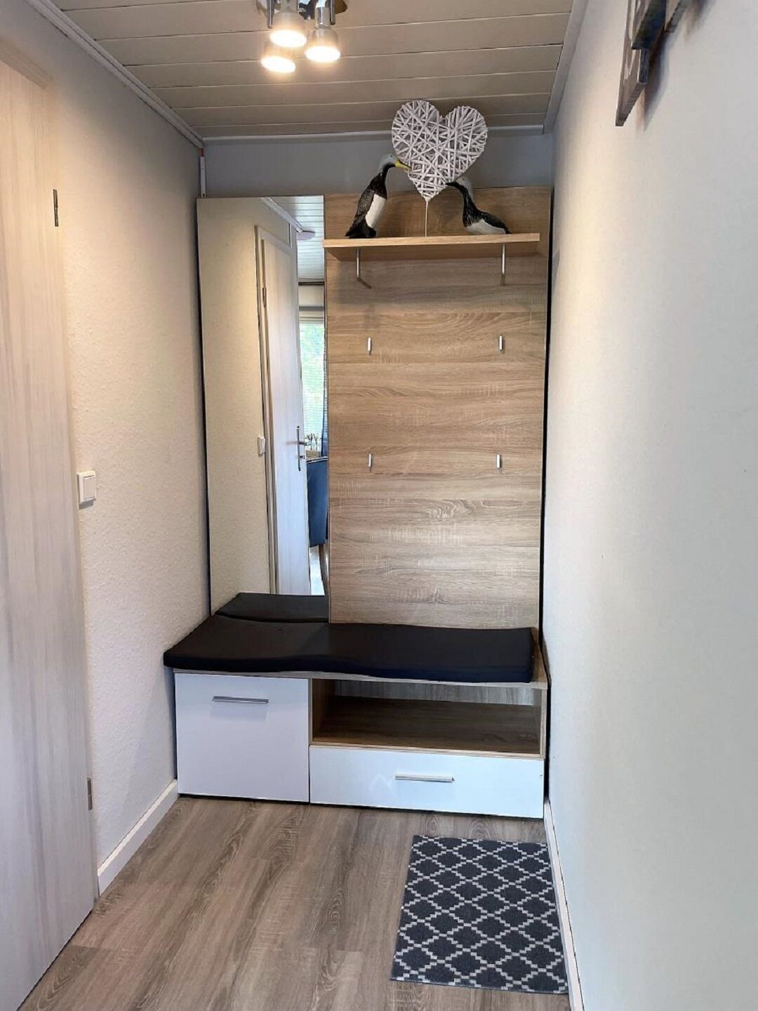 A compact room with a built-in bench, a small seating area, and a decorative heart-shaped wall piece.