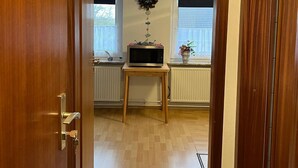 A hallway with a wooden door, a small wooden table with a microwave, and a wall-mounted clock.
