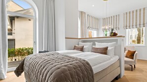 A modern bedroom with a large bed, a bedside table with a fruit bowl, and a view of the outside. - Luxury apartment with terrace, free SPA use and gym (Sylt)