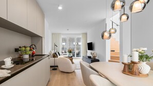 Une cuisine moderne dotée d’un îlot central, un coin repas avec une table et des chaises en bois, et un salon avec un canapé et un téléviseur.