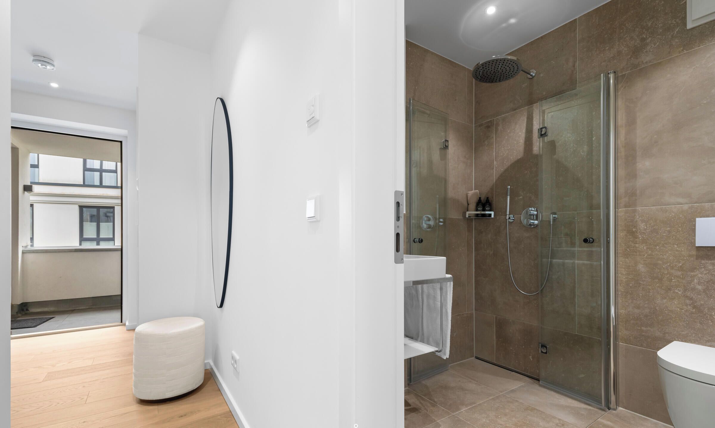 A modern bathroom with a glass shower enclosure, a white toilet, and a small white stool.