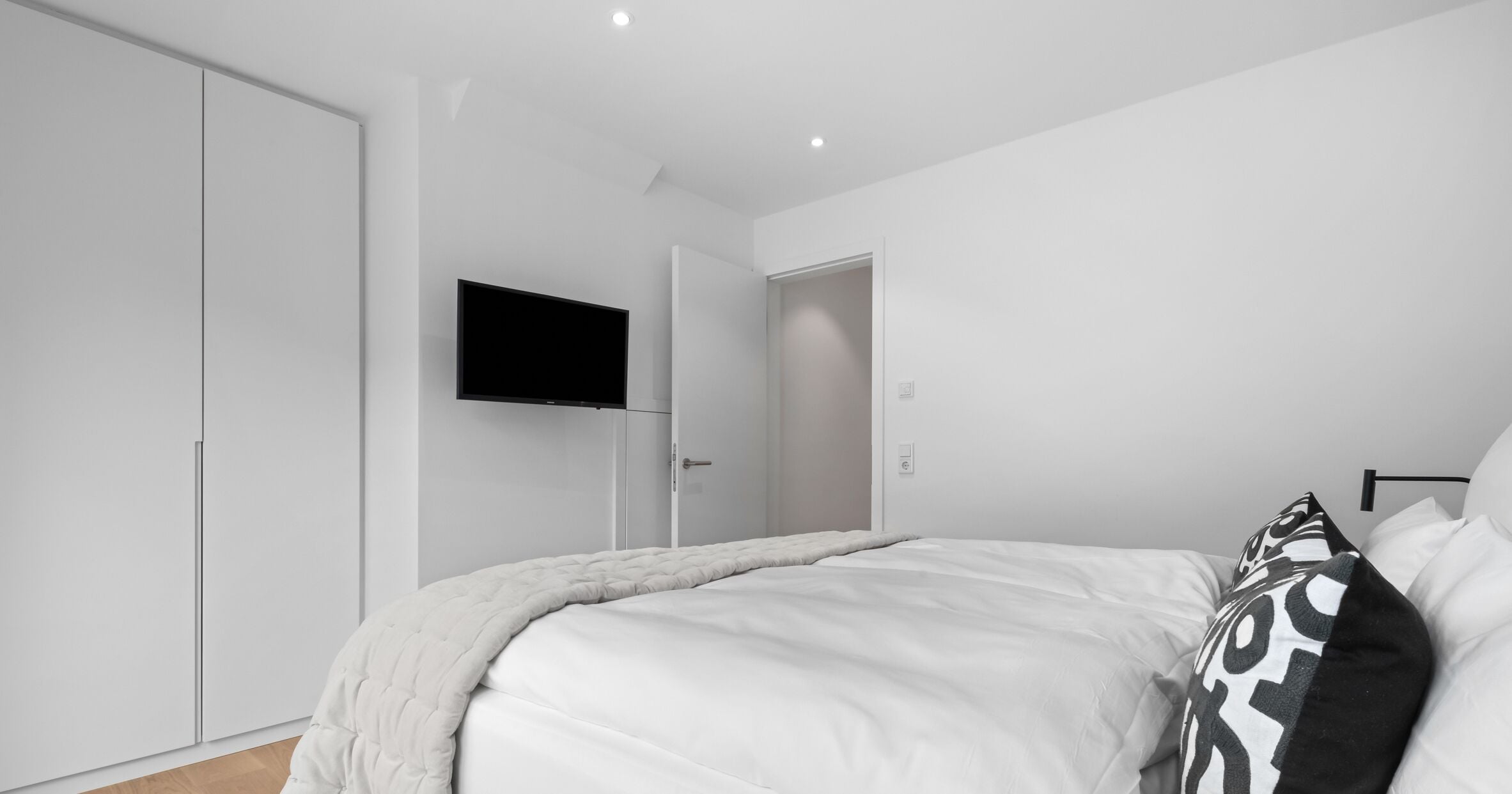 A modern bedroom with a bed, white wardrobe, and a flat-screen TV mounted on the wall.