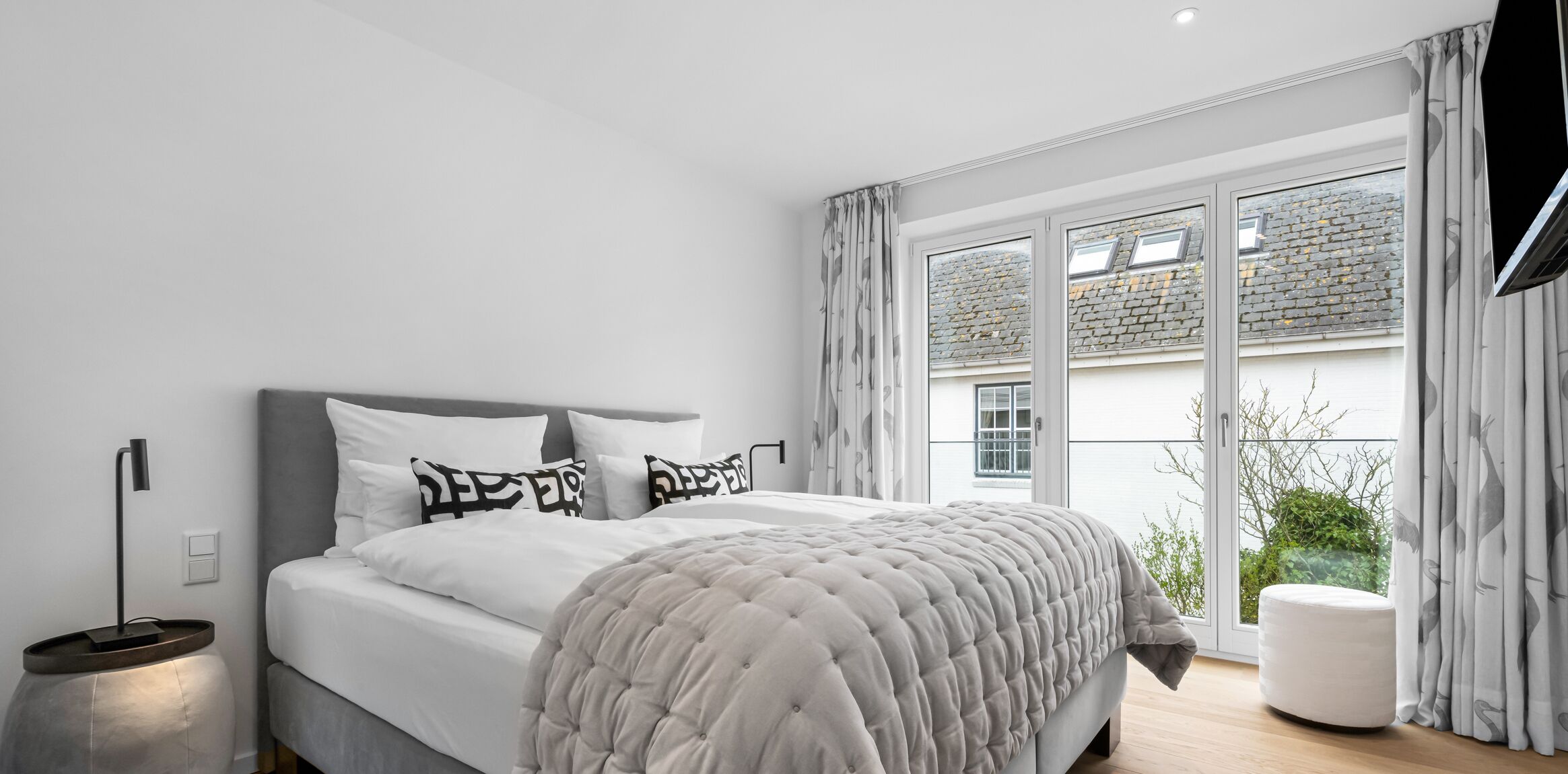 A modern bedroom with a bed, bedside table, and a view of the outside.