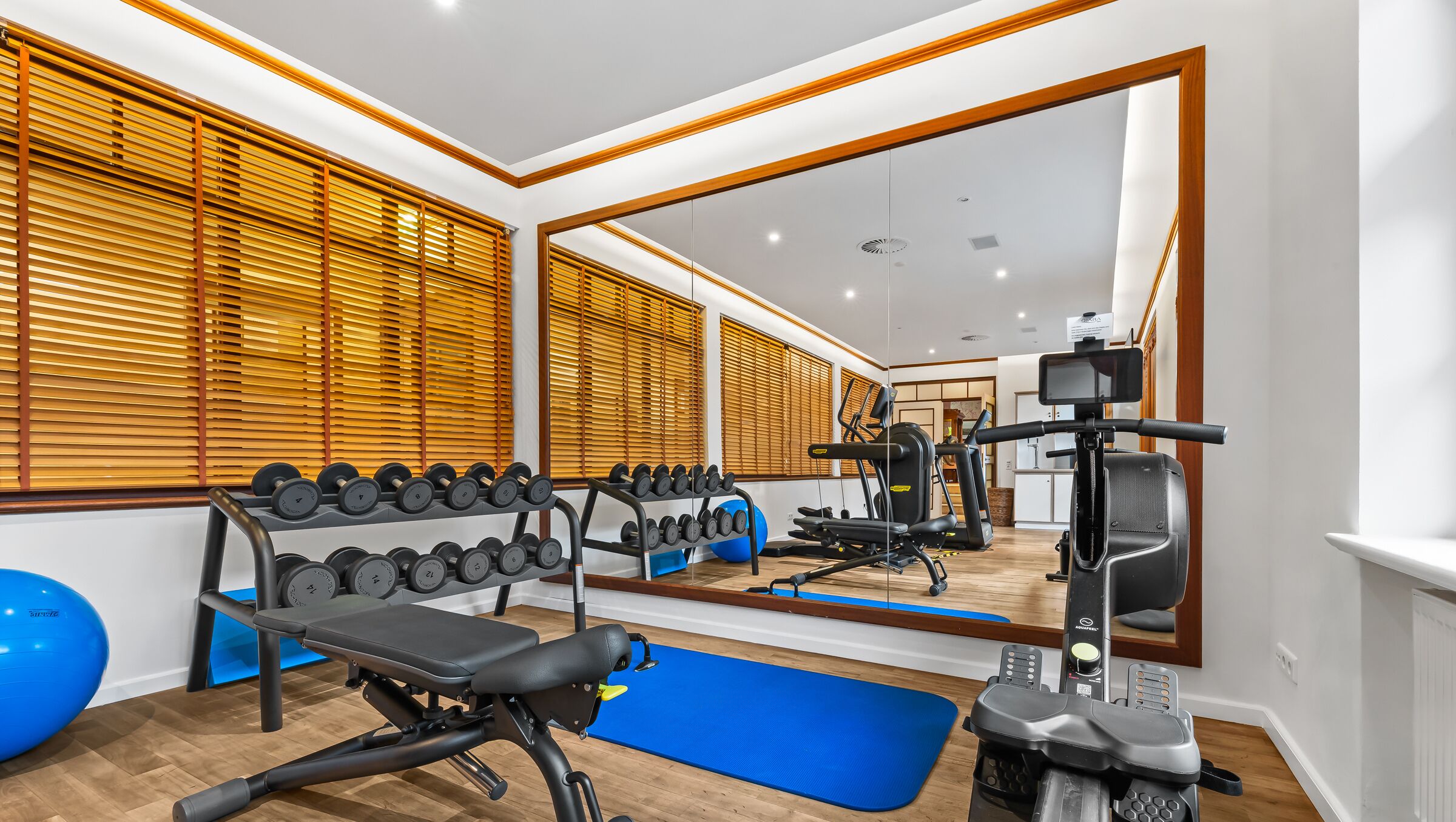 Een sportschool met trainingsapparatuur, een spiegel en houten zonwering.
