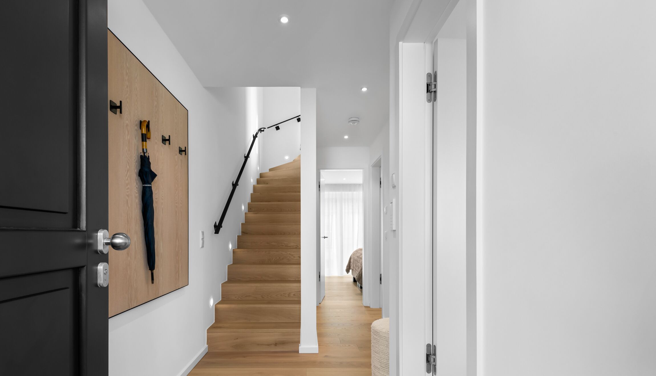 A modern interior with a wooden staircase, white walls, and a door with a black handle.