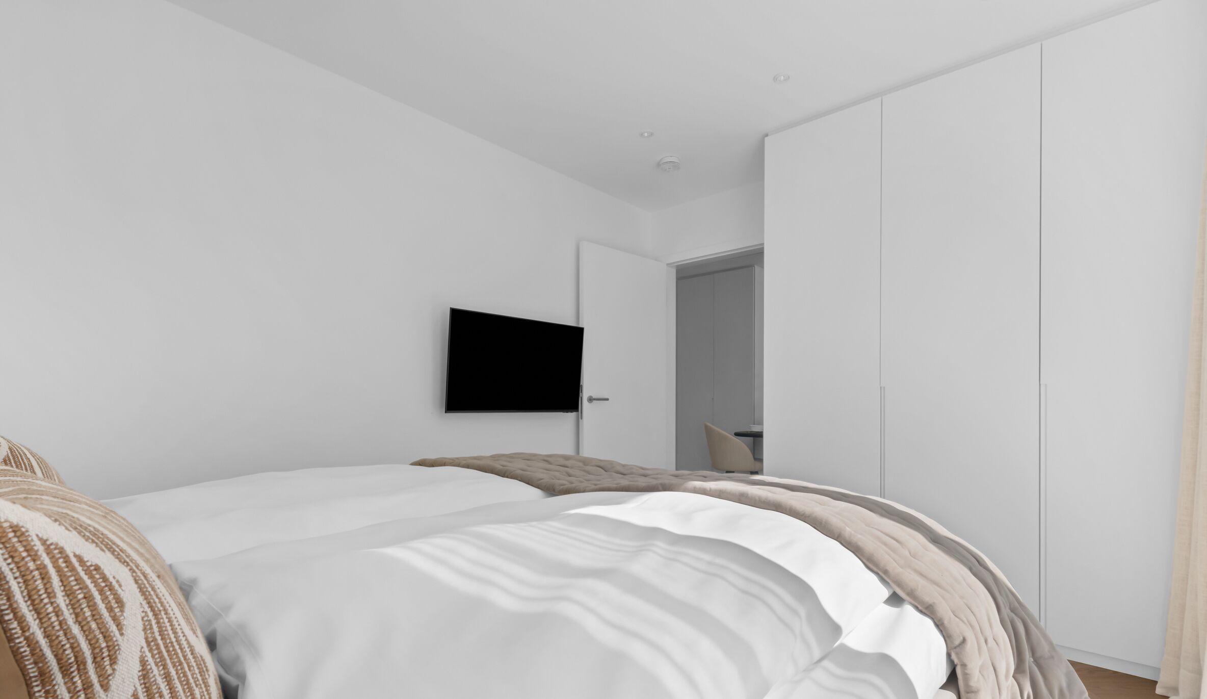 A modern bedroom with a bed, a flat-screen TV, and a wardrobe.