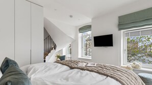 Een slaapkamer met een bed, een televisie, een raam en een trap.