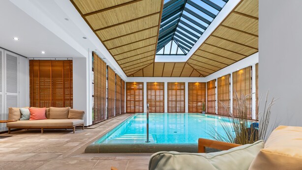 Een modern binnenzwembad met een glazen barrière, houten schuifdeuren en een hoge, lichtinlatende ruimte.
