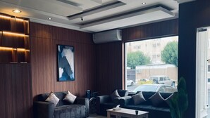 Eine moderne Lobby mit Wandverkleidung aus dunklem Holz, einem großen abstrakten Gemälde, einer schwarzen Ledersofa mit Kissen, einem Holztisch und einem großen Fenster mit Blick auf geparkte Autos.