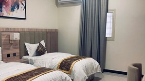 Ein Hotelzimmer mit zwei Betten, einem Kopfteil, einer Wandklimaanlage, einem Fenster mit Vorhängen und einem Bild an der Wand.