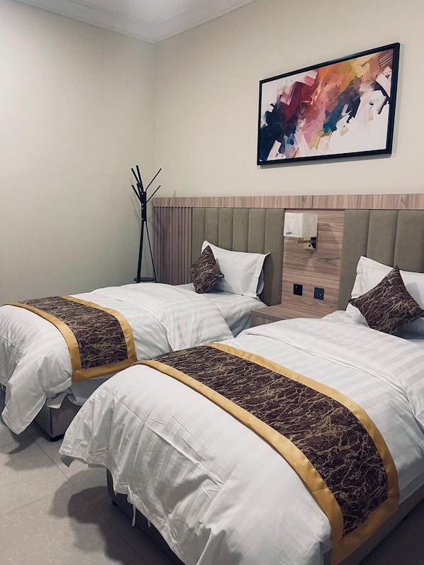Two plush beds with golden trim, a wooden nightstand, and a striking abstract painting adorn this inviting space.