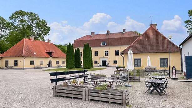 A building with a red-tiled roof, a yellow facade, and a gravel courtyard with outdoor seating. - 1 bedroom gorgeous home in Romakloster (Romakloster)