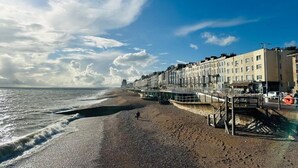 Une plage avec une promenade, des bâtiments et une personne qui se promène.
