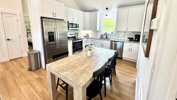 A modern kitchen with white cabinets, stainless steel appliances, and a wooden dining table.