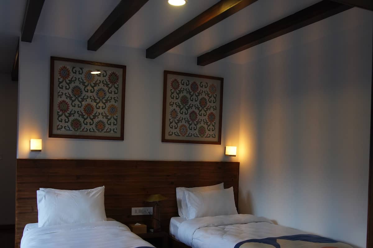 A hotel room with two beds, wooden beams on the ceiling, and two wall-mounted lamps.
