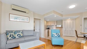 Ein modernes Wohnzimmer mit grauem Sofa und blauem Sessel, einem weißen Couchtisch sowie einer Küche im Hintergrund.