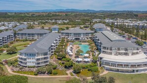 Ein modernes Resort mit mehreren Gebäuden, einem zentral gelegenen Pool und umgebender Bepflanzung.