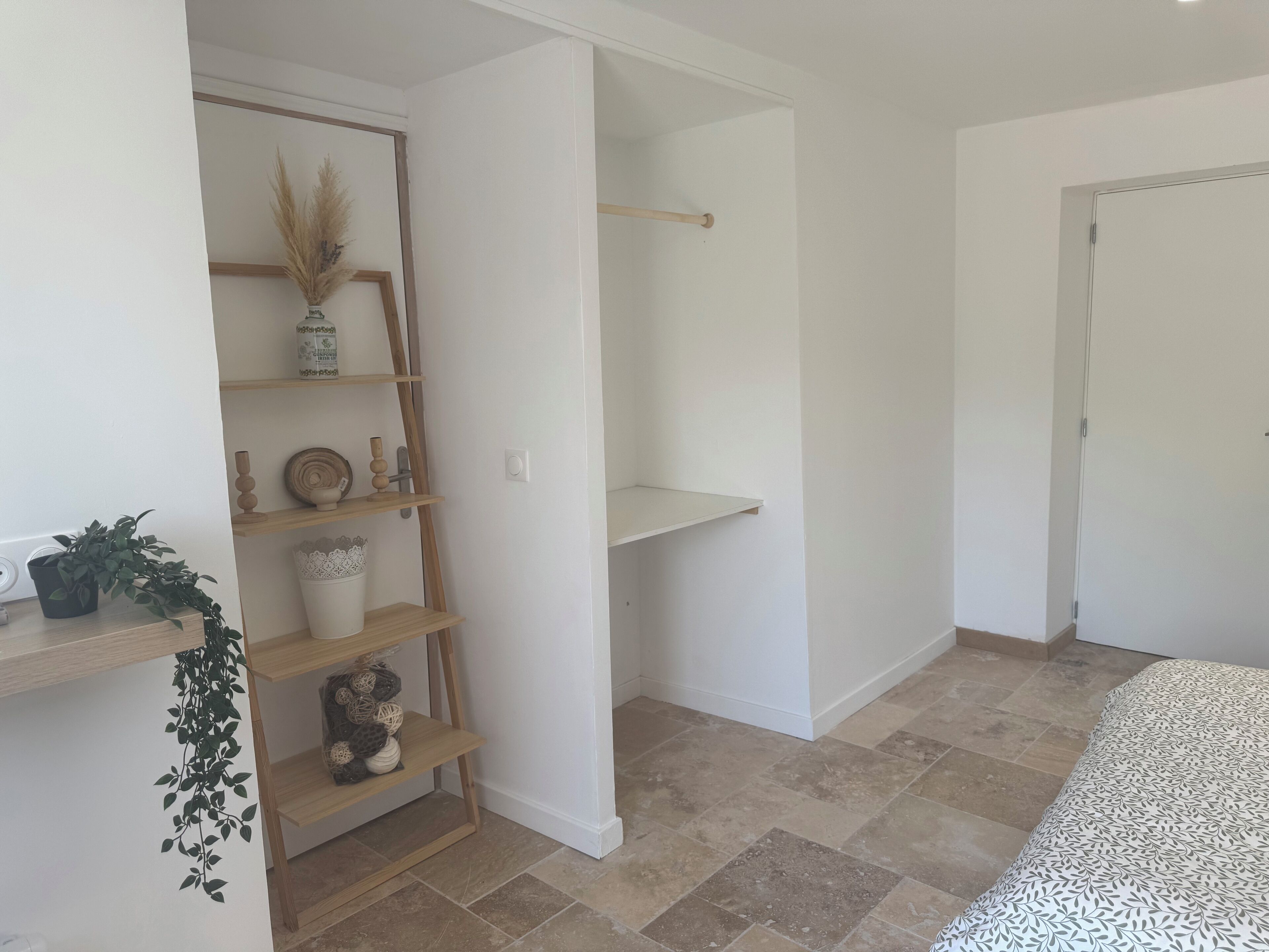 A room with a wooden shelf unit, a bed with a patterned bedspread, and a tiled floor.