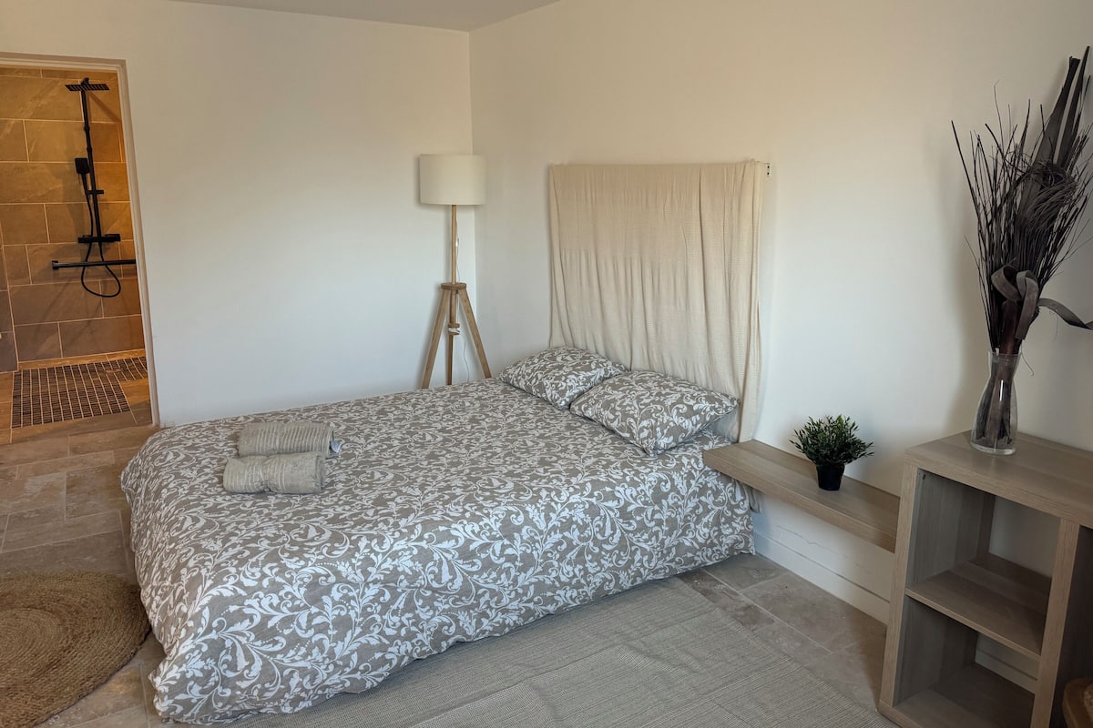 A bedroom with a bed, a floor lamp, a curtain, a small plant, and a wooden nightstand.