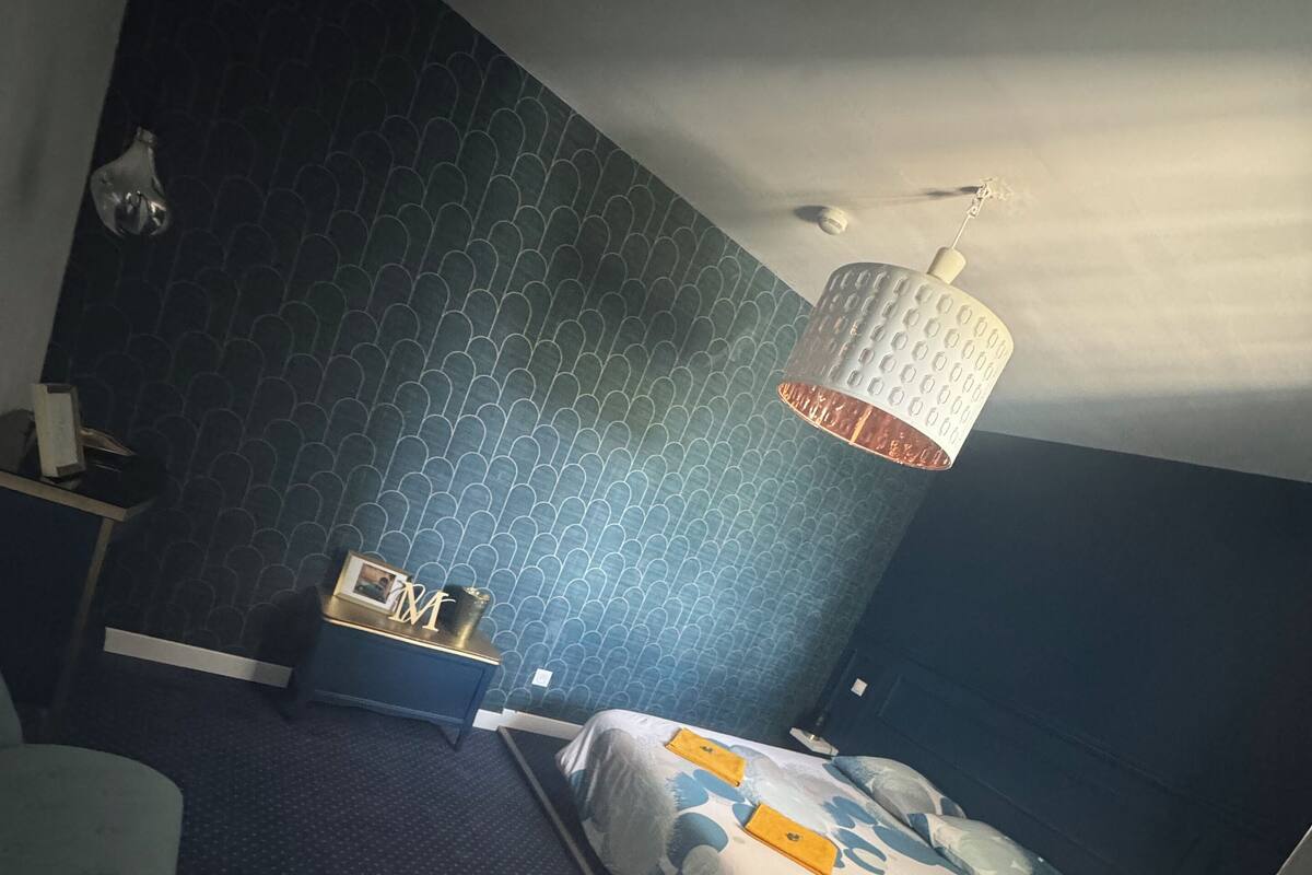 A bedroom with a bed, a desk, a chair, and a hanging light fixture.