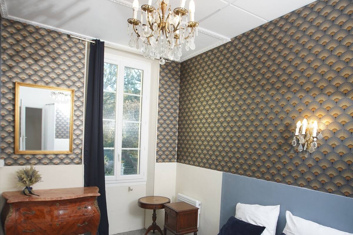 A bedroom with a large bed, a dresser, a mirror, a chandelier, and a patterned wall.