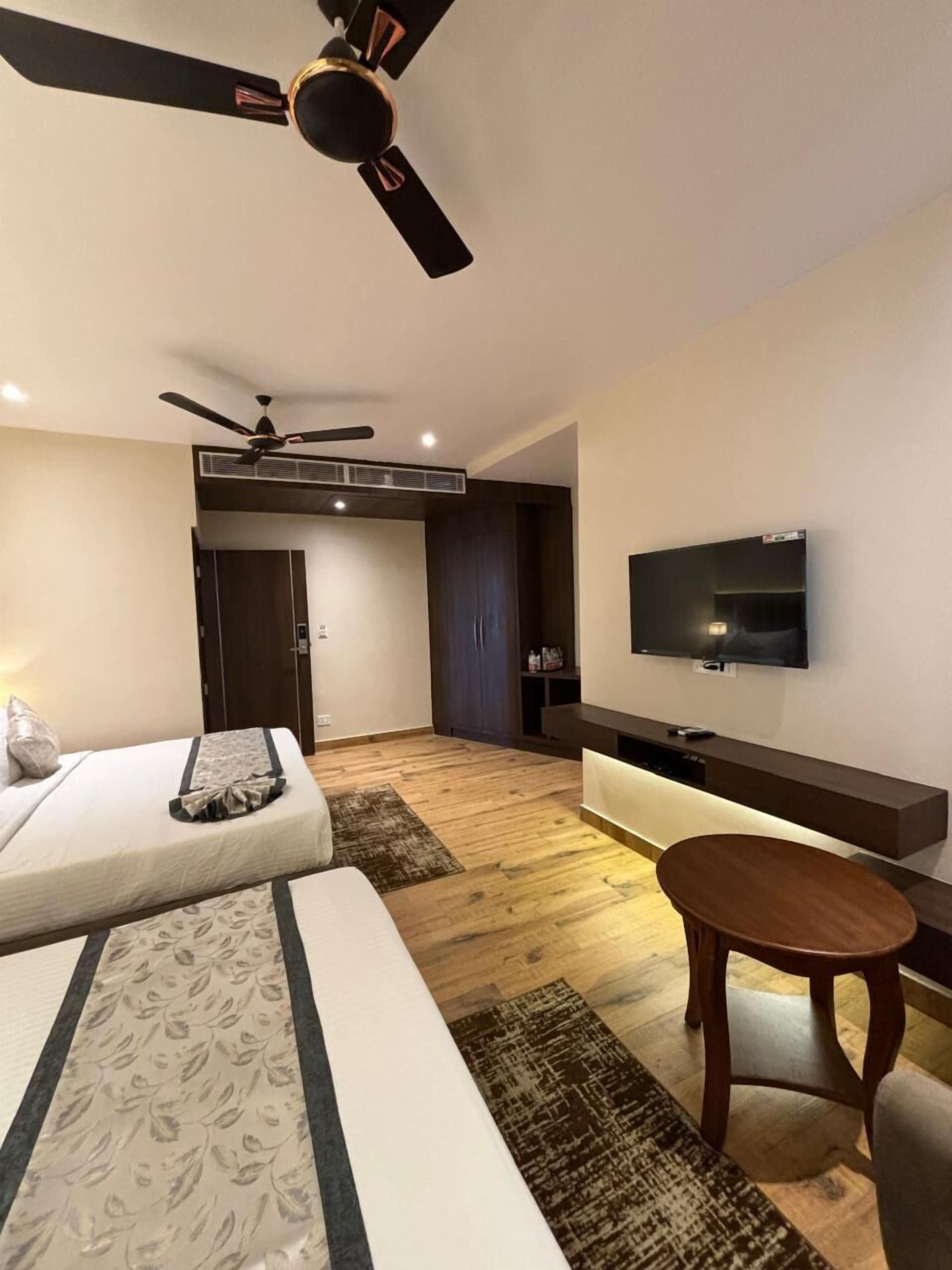 A modern hotel room with a bed, a small table, a TV mounted on the wall, and a ceiling fan.