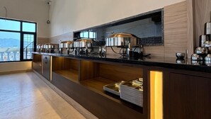 A modern kitchen with a long counter, stainless steel appliances, and a view of the city. - Shri Bhagwan Gopi Dham Dharmsala (Haridwar)