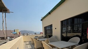 A rooftop terrace with checkered flooring, wicker furniture, and a view of distant mountains. - Shri Bhagwan Gopi Dham Dharmsala (Haridwar)