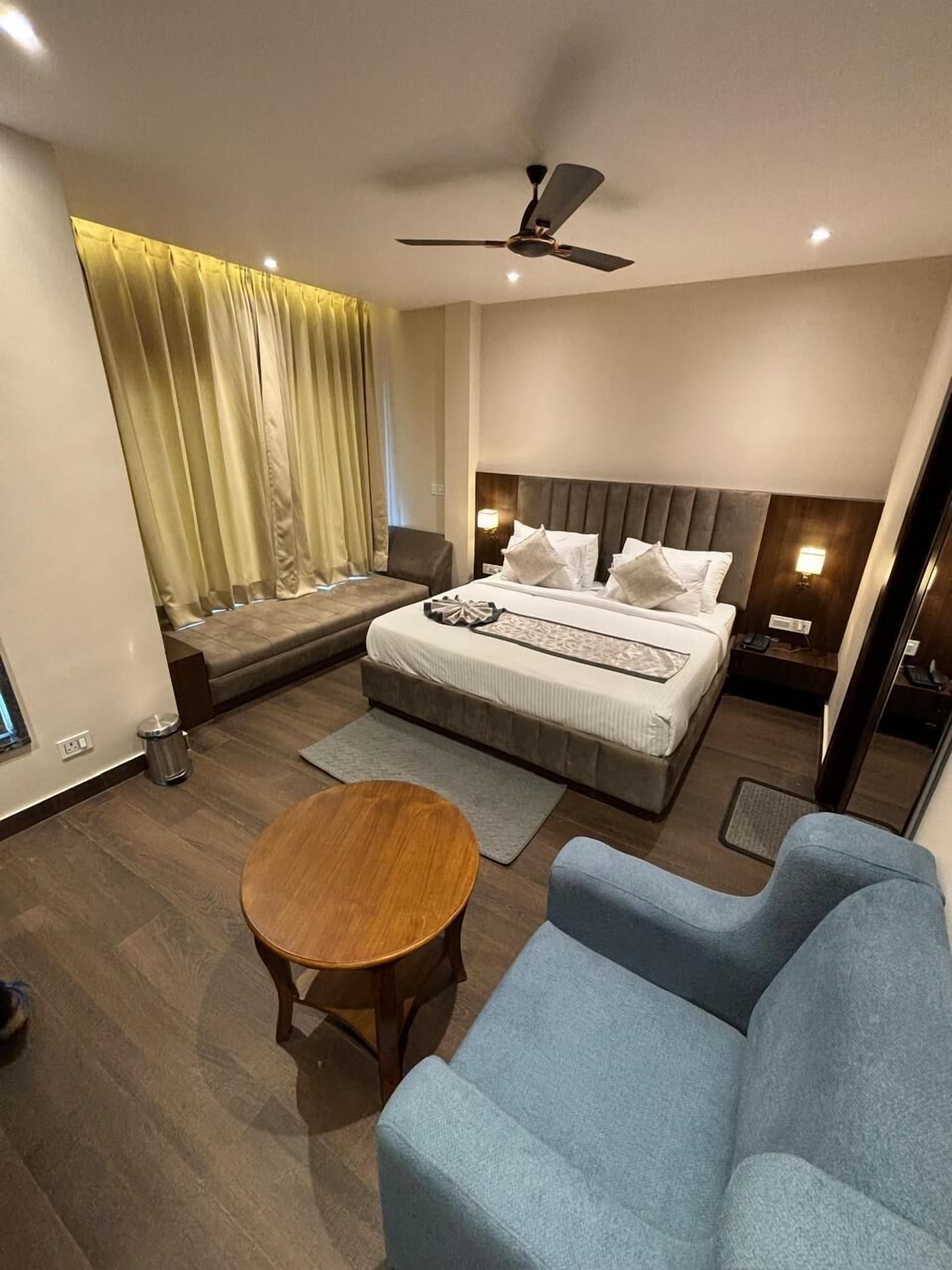 Ein modernes Hotelzimmer mit einem großen Bett, einer Sitzecke mit einer Couch und einem kleinen Tisch sowie einem Deckenventilator.