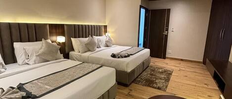 A modern hotel room with two beds, a ceiling fan, a small round table, and a view of the outside.