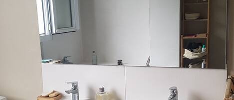 Une salle de bain avec deux lavabos, un miroir et une étagère contenant des articles de toilette.