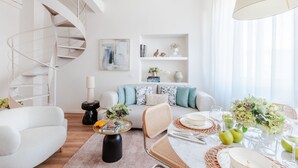 A modern living room with a spiral staircase, a sofa with patterned cushions, a dining table set for four, and a bookshelf with decorative items. - Letizia Penthouse in Lucca (Lucca)