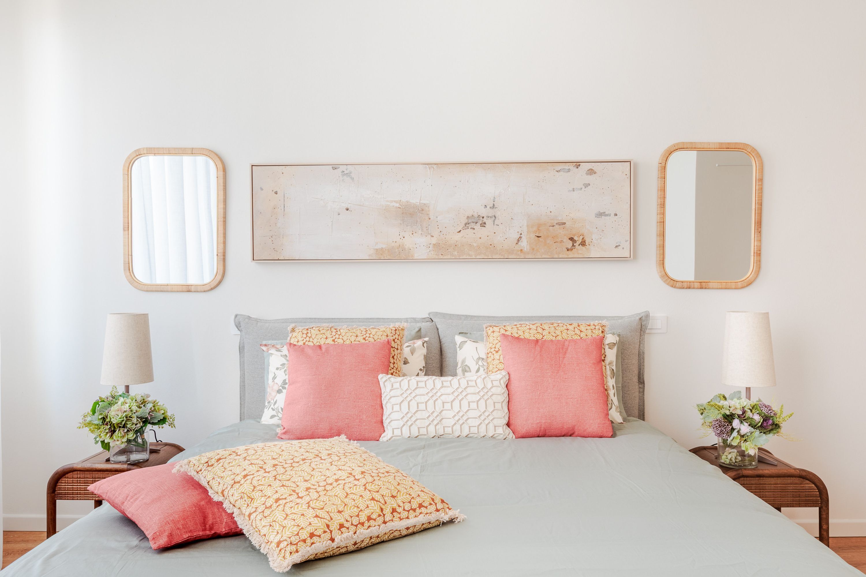 Ein Schlafzimmer mit einem Bett, Kissen, einem Nachttisch, einer Lampe und einem an der Wand befestigten Spiegel.