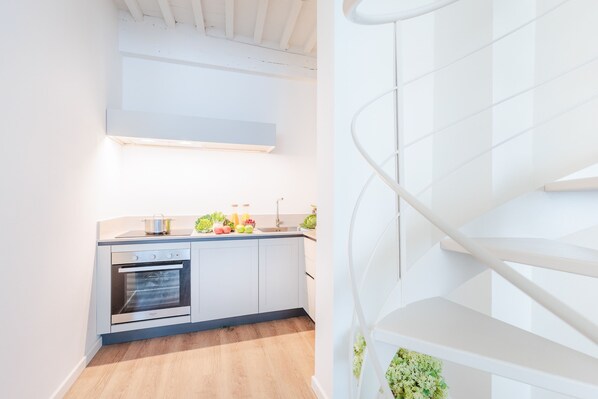 A modern kitchen with white cabinetry, a built-in oven, and a spiral staircase with a white railing. - Letizia Penthouse in Lucca (Lucca)