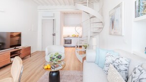A modern living room with a sofa, coffee table, and a TV. A spiral staircase leads to a kitchen area. - Letizia Penthouse in Lucca (Lucca)