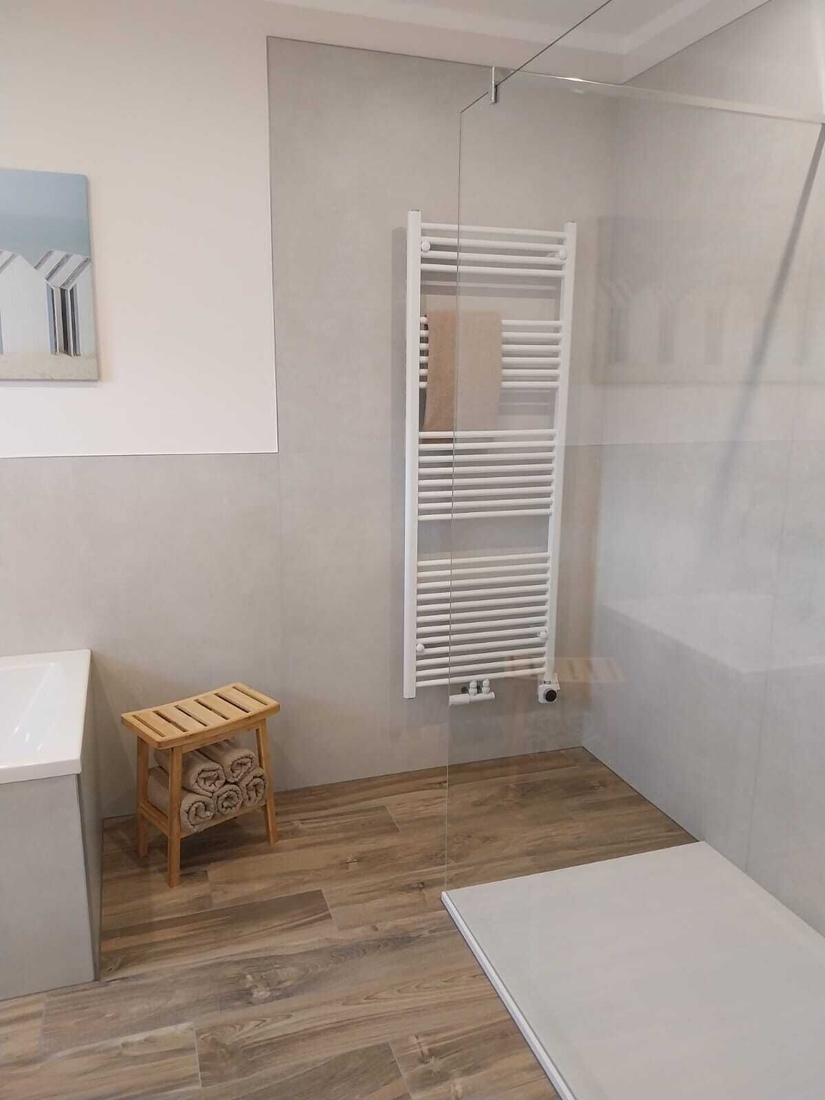 Een badkamer met een witte radiator, een houten kruk met handdoeken en een witte wastafel.