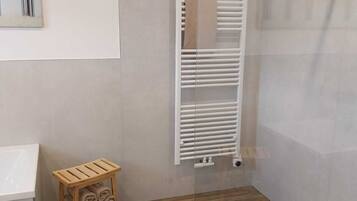 Een badkamer met een witte radiator, een houten kruk met handdoeken en een witte wastafel.