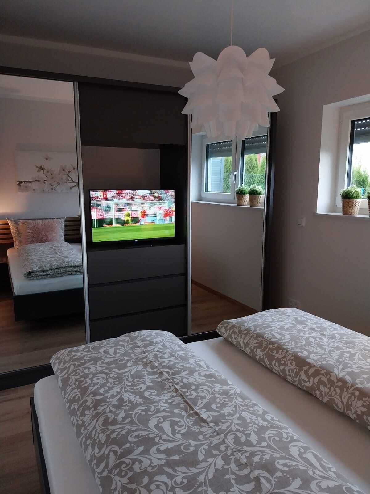 Une chambre moderne avec un lit, une télévision, une porte coulissante et une fenêtre agrémentée de plantes.