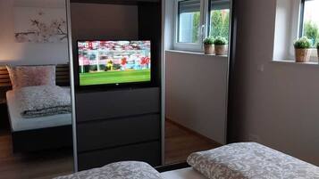 Une chambre moderne avec un lit, une télévision, une porte coulissante et une fenêtre agrémentée de plantes.