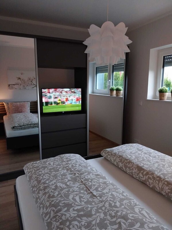 A modern bedroom with a bed, a TV, a sliding door, and a window with plants.