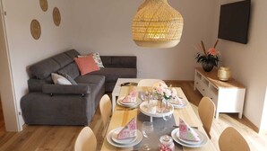 Una sala de estar moderna con un sofá gris, una mesa de comedor preparada para cuatro personas y una lámpara colgante de fibra.