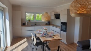 Una cocina moderna con comedor, ventanas amplias y una lámpara colgante.