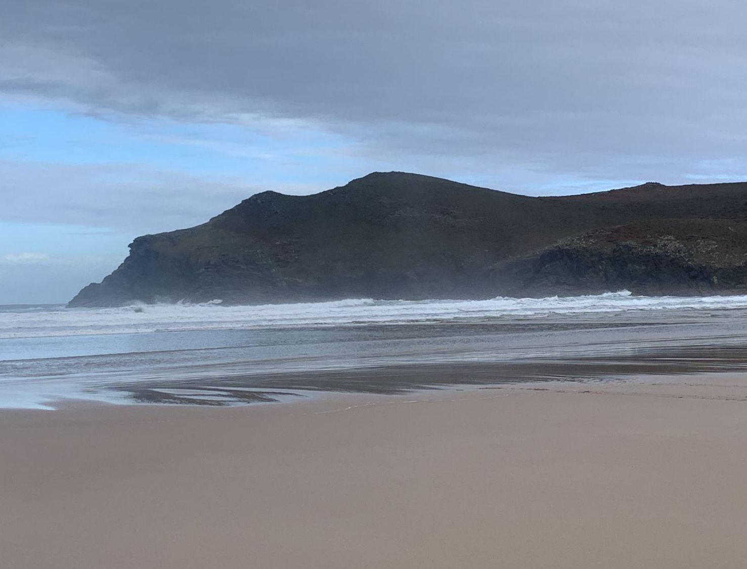 Una spiaggia con una scogliera rocciosa e onde che si infrangono sulla riva.