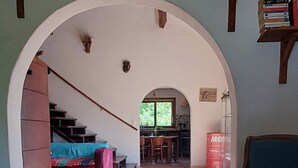 A spacious living area with a tiled floor, a blue sofa, a wooden bookshelf, and a staircase leading to another room. - Sunset House - Secluded house with panoramic sunset views. (Lahitère)