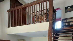 A wooden staircase with a cushioned bench at the bottom. A wooden railing and a bookshelf are visible in the background. - Sunset House - Secluded house with panoramic sunset views. (Lahitère)