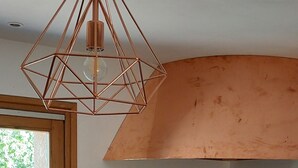 A kitchen with a gas stove, wooden cabinets, a backsplash with a terrazzo pattern, and a hanging copper pendant light. - Sunset House - Secluded house with panoramic sunset views. (Lahitère)