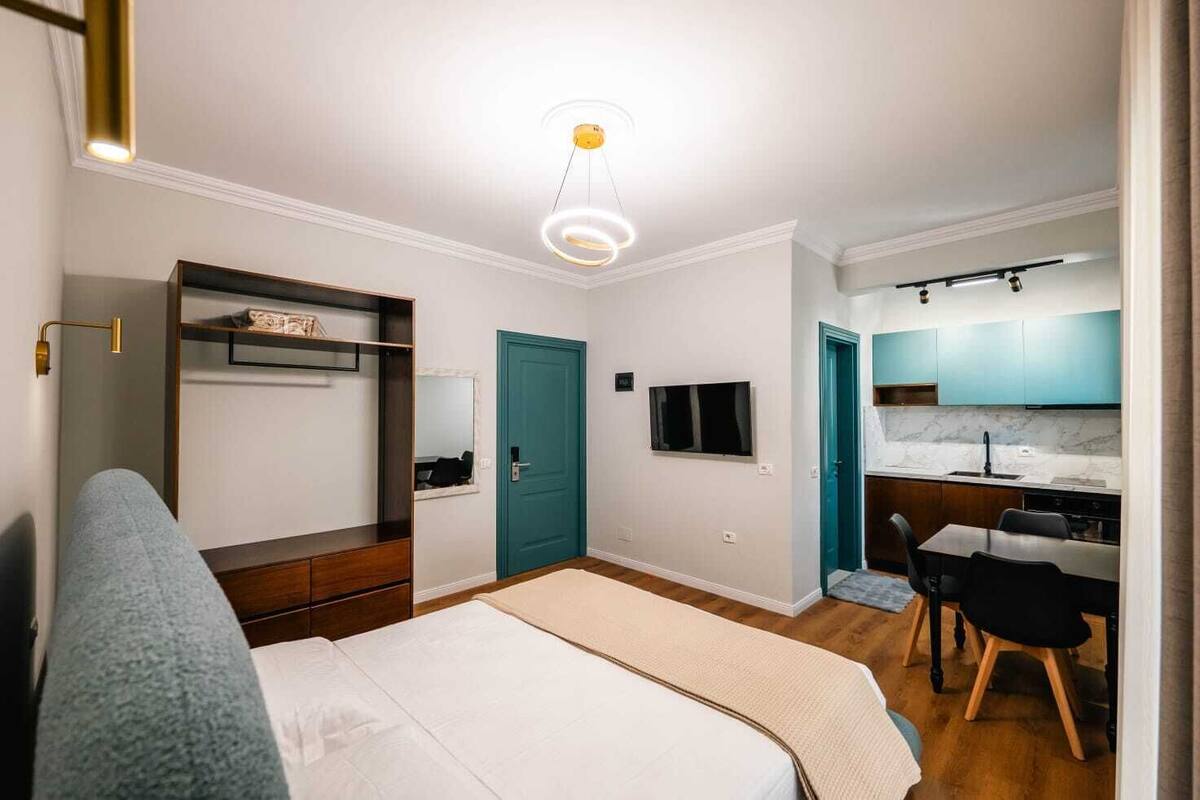 A bedroom with a bed, a wardrobe, a desk, and a kitchenette.