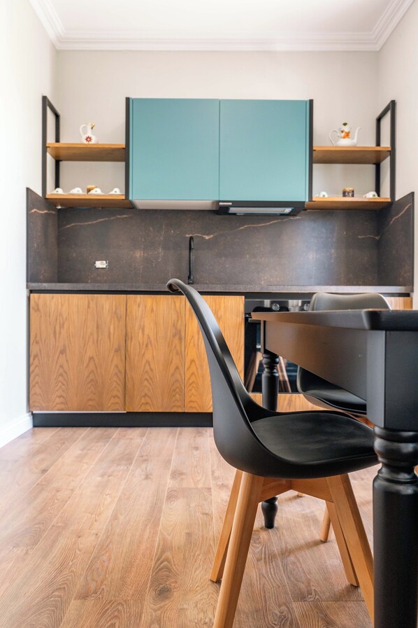 Una cucina moderna con mobili color petrolio, mensole in legno e una sedia nera.